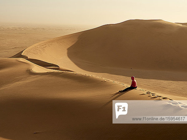 Frau sitzt allein auf dem Kamm einer Düne in der Wüste  Walvis Bay  Namibia