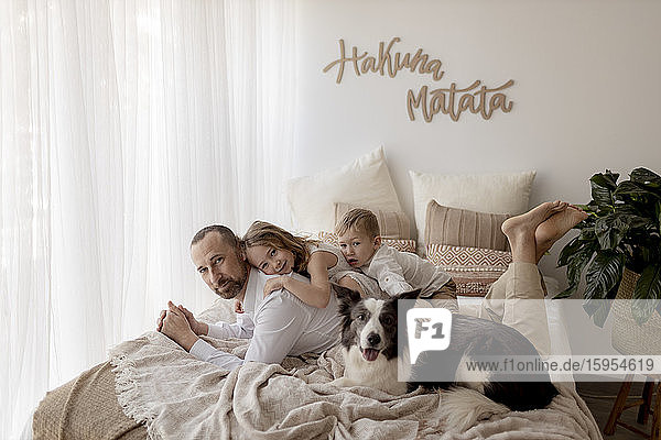 Portrait of father lying on bed with his two children and dog