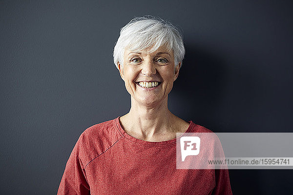 Porträt einer glücklichen älteren Frau mit rotem Hemd vor grauer Wand
