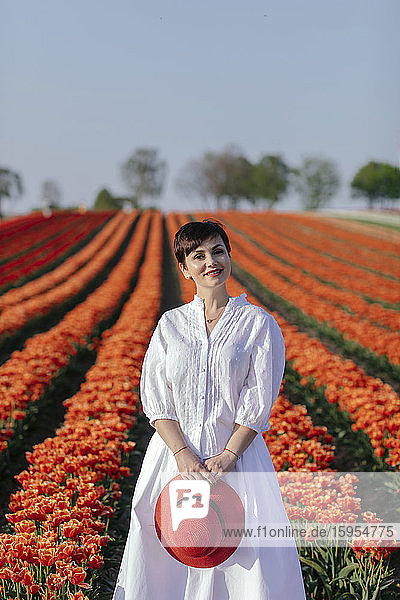 Bildnis einer lächelnden  weiss gekleideten Frau vor einem Tulpenfeld stehend