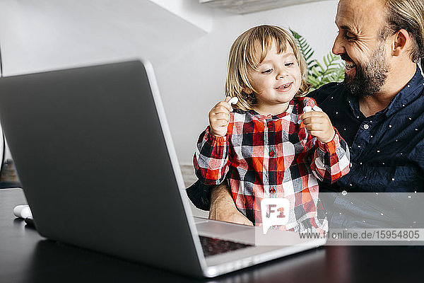 Glücklicher Vater mit Tochter bei einem Videochat am Schreibtisch