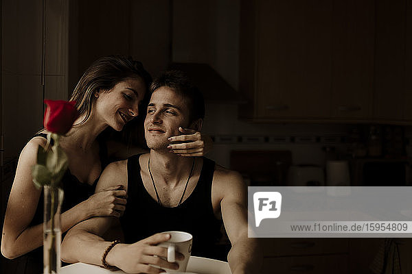 Romantisches junges Paar mit roter Rose am Küchentisch sitzend