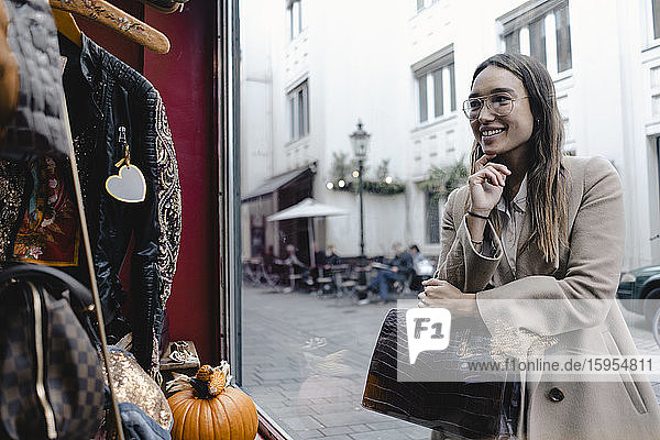 Lächelnde mittelgroße erwachsene Frau betrachtet Schaufensterauslage eines Geschäfts in der Stadt