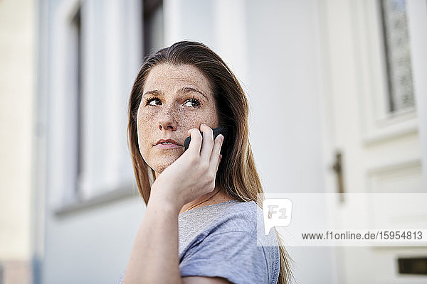 Frau schaut weg  während sie am Smartphone gegen das Haus spricht