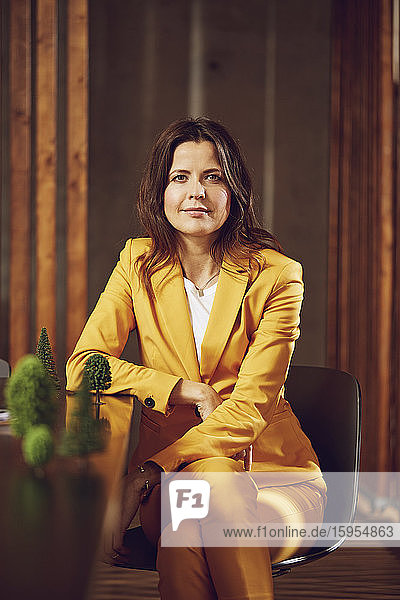 Portrait of businesswoman wearing yellow suit sitting at desk in office