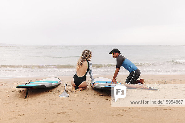 Instructor and woman kneeling while talking by paddleboards at beach