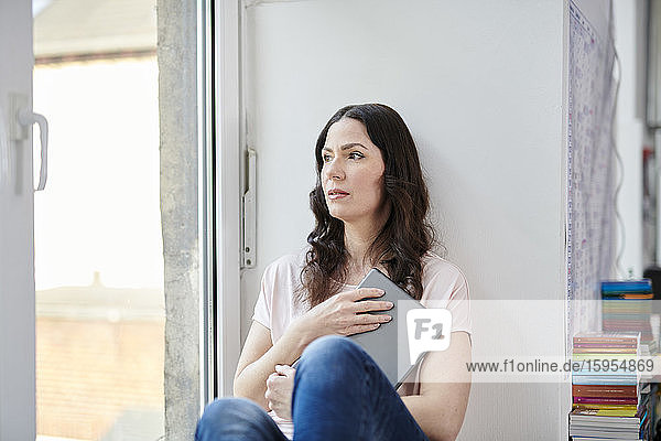 Thoughtful businesswoman with digital tablet looking through window at office
