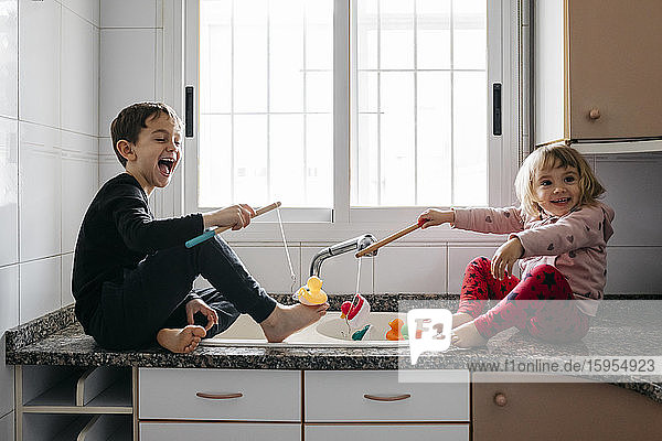 Boy and his little sister fishing rubber ducks in kitchen sink