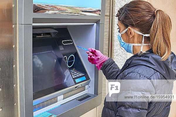 Frau trägt Maske und benutzt Kreditkarte am Geldautomaten während einer Pandemie