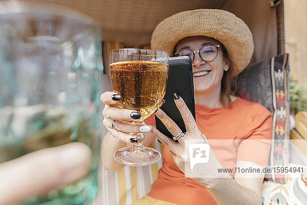 Glückliche reife Frau auf der Terrasse  die ein Glas Limonade mit einem Smartphone fotografiert