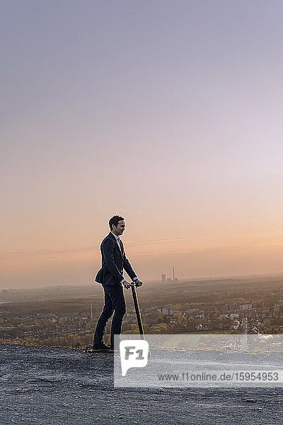 Mature businessman riding a kick scooter on a disused mine tip at sunset