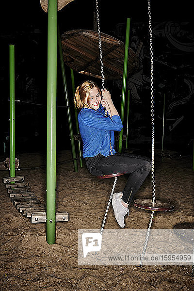 Glückliche junge Frau in voller Länge spielt nachts auf dem Spielplatz