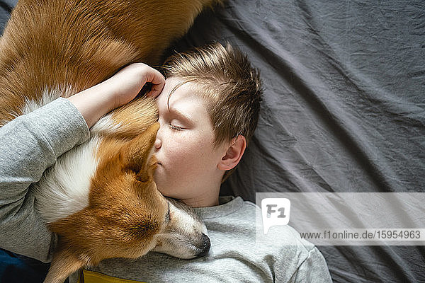 Portrait of boy lying on bed cuddling his dog