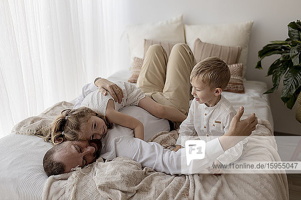 Vater liegt im Bett und kuschelt mit seinen beiden Kindern