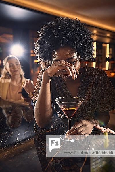 Fröhliche Frau trinkt einen Cocktail in einer Bar