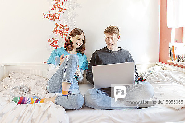 Portrait of teenage couple sitting together on bed learning with laptop