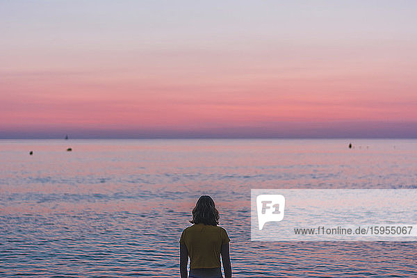 Rückansicht einer Teenagerin  die bei Sonnenaufgang auf den Horizont über dem Meer schaut