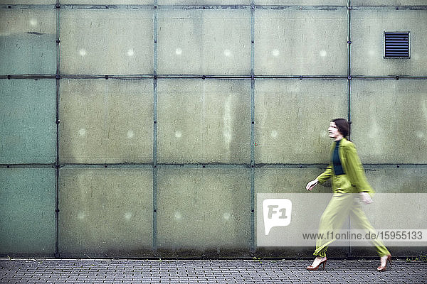 Geschäftsfrau im grünen Anzug beim Passieren einer Mauer