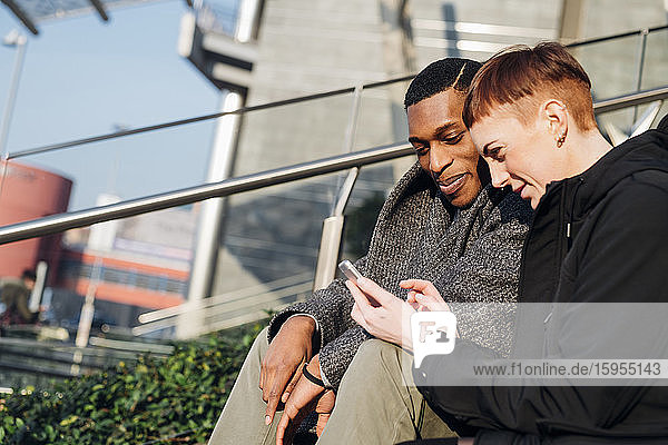 Junges Paar in der Stadt sitzt auf einer Treppe und benutzt ein Handy