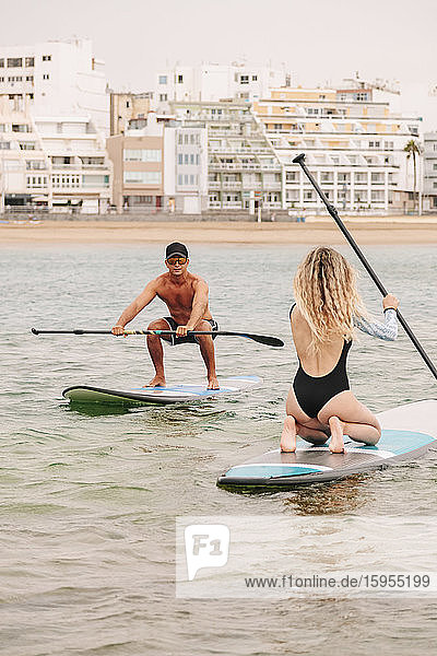 Instructor and young woman paddleboarding on sea