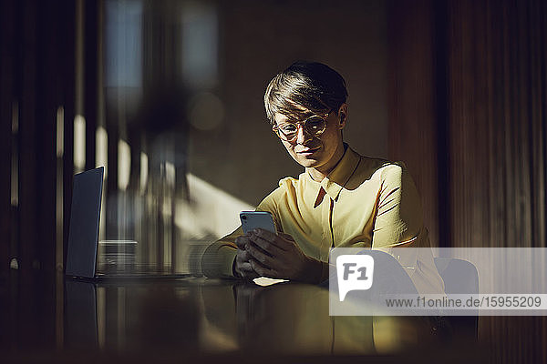 Geschäftsfrau  die in ihrem nachhaltigen Büro sitzt und ein Smartphone benutzt