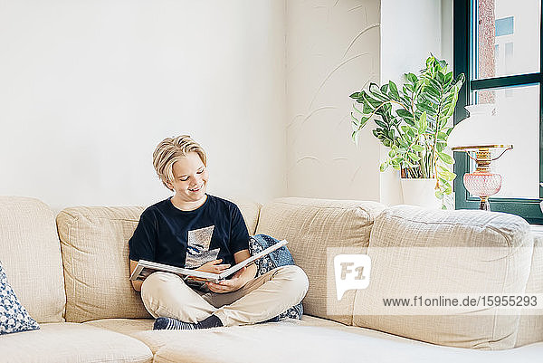 Happy boy sitting on couch in living room at home reading a book