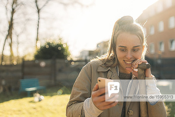 Junge Frau benutzt Smartphone im Garten bei Sonnenschein