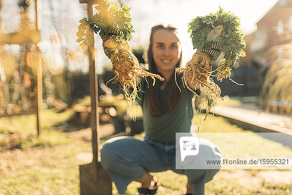 Proud young woman holding celeriac in garden