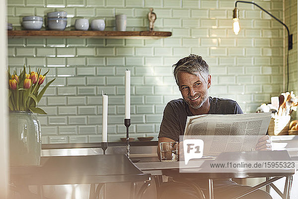Lächelnder reifer Mann sitzt in der Küche und liest Zeitung