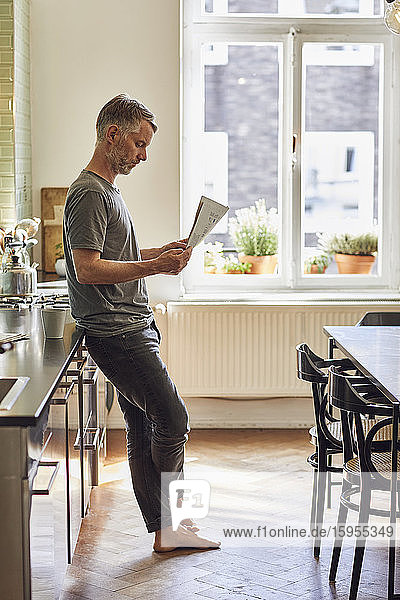 Reifer Mann liest zu Hause in der Küche Zeitung