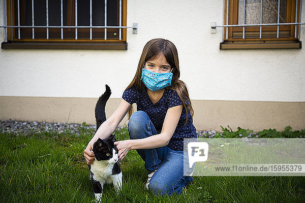 Mädchen trägt Schutzmaske und streichelt ihre Katze im Garten