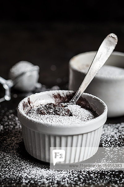 Studioaufnahme eines Bechers mit geschmolzenem Schokoladenkuchen mit Puderzucker