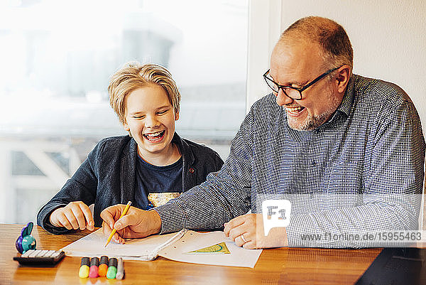 Glückliche Vater und Sohn machen am Schreibtisch Hausaufgaben