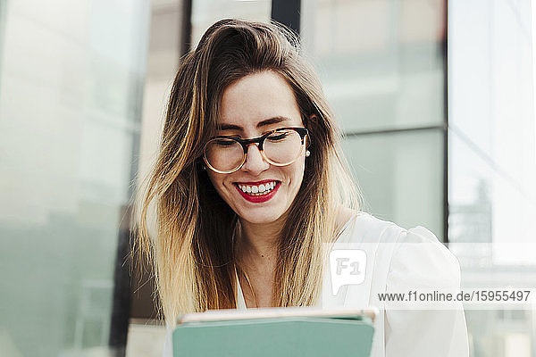 Porträt einer lächelnden jungen Geschäftsfrau  die ein digitales Tablet im Freien benutzt