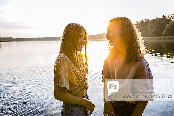 Lächelnde Freunde stehen bei Sonnenuntergang gemeinsam am See