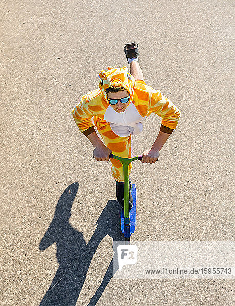 Junger Mann trägt Giraffenkostüm auf Roller von oben