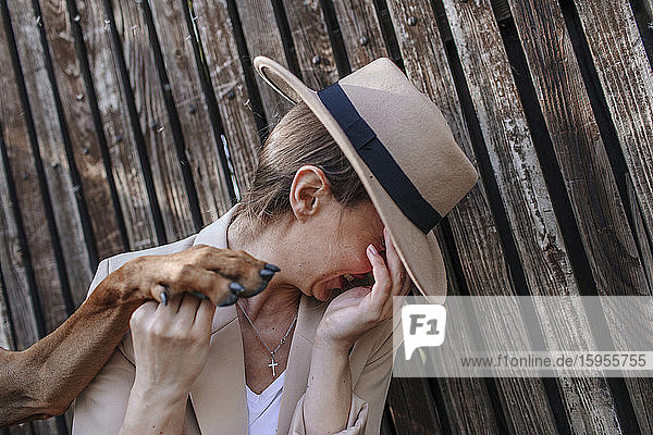 Lachende Frau mit Hut  die die Pfote ihres Hundes hält