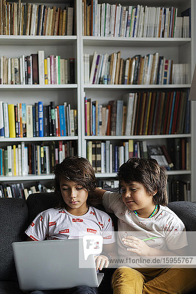 Jungen sitzen mit Laptop auf dem Sofa vor dem Bücherregal im Wohnzimmer zu Hause
