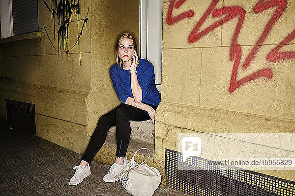 Junge Frau  die nachts in der Stadt auf einer Treppe sitzt und mit ihrem Handy telefoniert