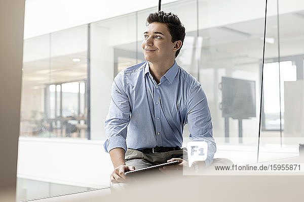 Porträt eines lächelnden jungen Geschäftsmannes mit Tablette am Fenster im Büro