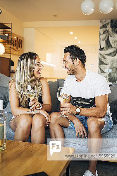 Laughing couple sitting on the couch with glasses of white wine
