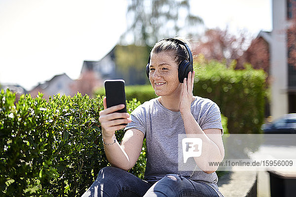 Lächelnde Frau hört Musik über Kopfhörer auf einem Smartphone bei Pflanzen