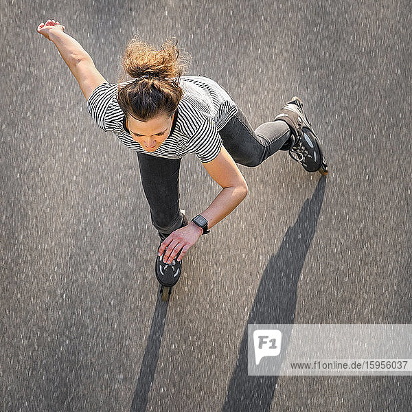 Hochwinkelaufnahme einer Frau  die im Sommer auf der Straße Inline-Skates fährt