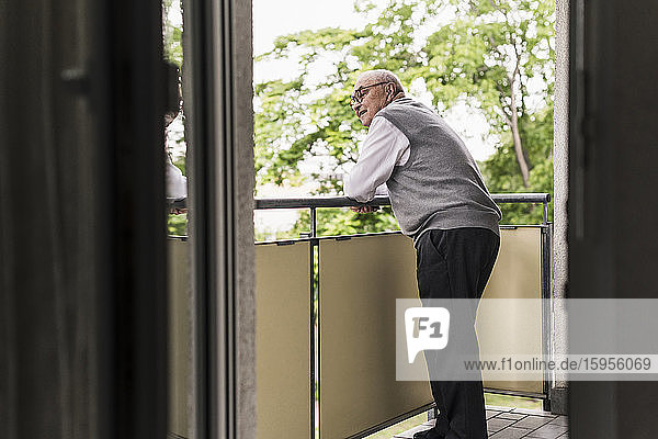 Neugieriger älterer Mann steht auf dem Balkon und beobachtet etwas