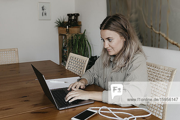 Frau benutzt Laptop  während sie während der Quarantäne zu Hause am Tisch im Esszimmer sitzt
