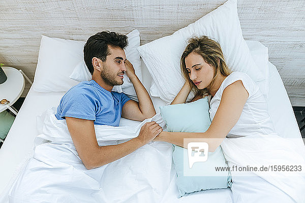 Lächelnder Mann sieht Partner an  der zu Hause auf dem Bett schläft