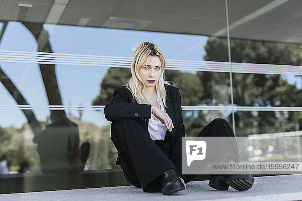 Porträt einer jungen Geschäftsfrau mit gefärbten blonden Haaren vor einem Bürogebäude sitzend