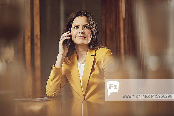 Geschäftsfrau am Telefon im gelben Anzug am Schreibtisch im Büro sitzend