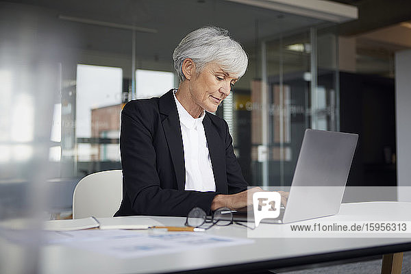 Leitende Geschäftsfrau sitzt am Schreibtisch und arbeitet am Laptop