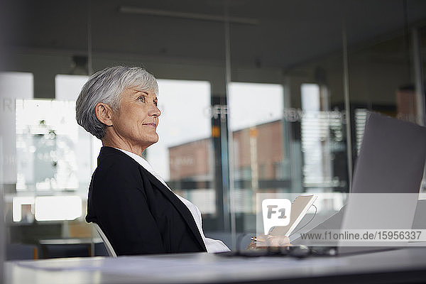 Ältere Geschäftsfrau sitzt am Schreibtisch im Büro und schaut in die Ferne